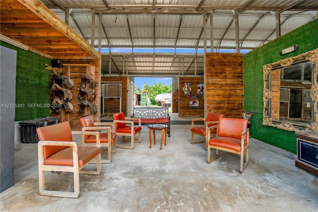Covered equestrian facility featuring wood-paneled walls, concrete flooring, artificial turf accents, and built-in stall partitioning