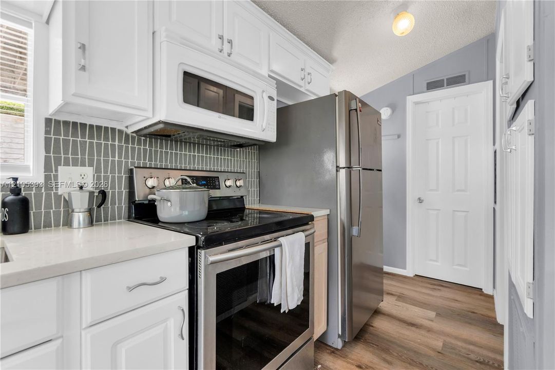 Kitchen featuring white cabinetry, wood-finish flooring, stone-surface countertops, stainless steel appliances, and a patterned tile backsplash