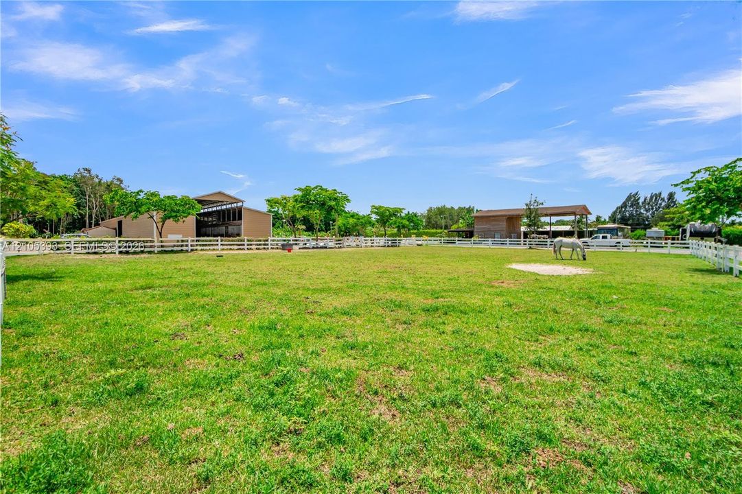 Expansive pasture featuring white post-and-rail fencing, multiple outbuildings, and mature trees
