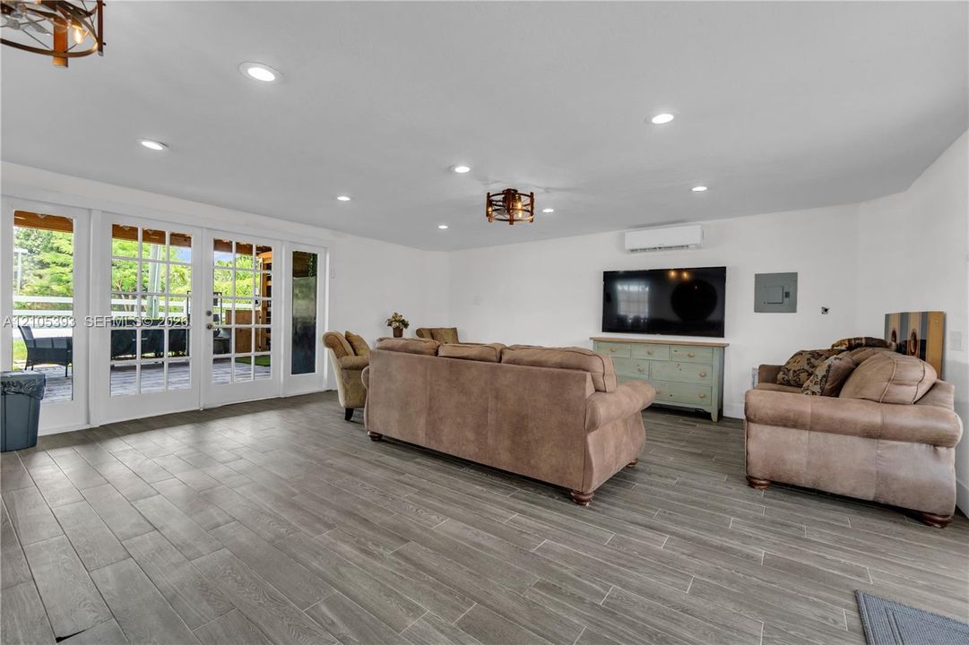 Open-concept space featuring wood-finish tile flooring, recessed lighting, wall-mounted ductless climate control system, and dual French door entryways