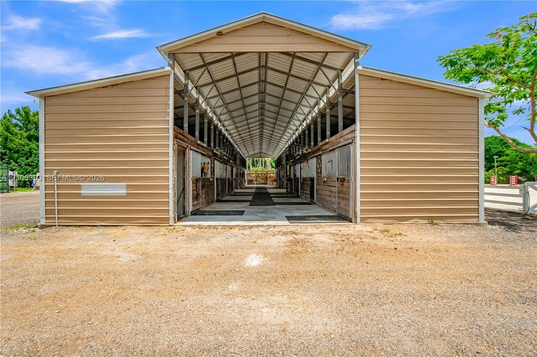 Stable building featuring metal siding, a peaked roof with exposed rafters, multiple stalls, and a concrete central aisle