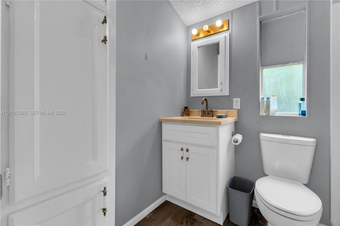 Bathroom featuring a white vanity cabinet with a wood-finish countertop, brushed metal hardware, wall-mounted medicine cabinet, and three-light vanity fixture