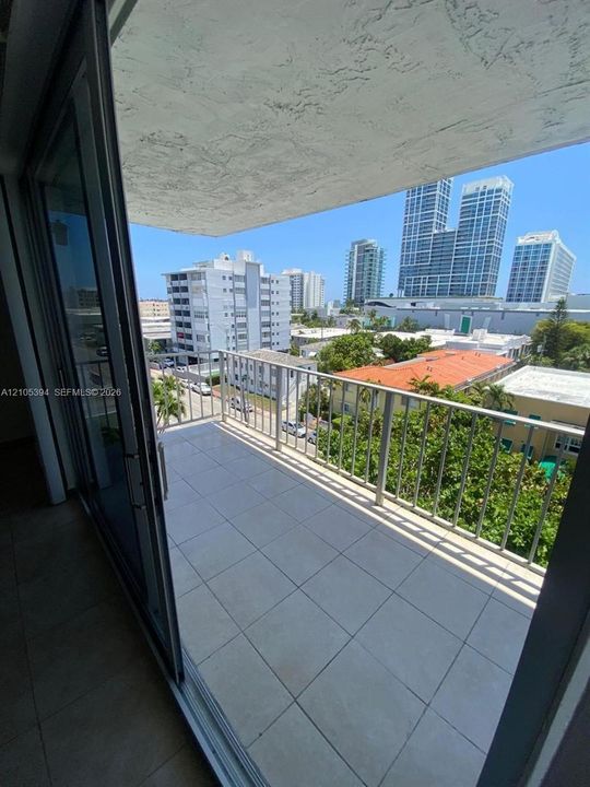 Balcony with tile flooring and metal railings, featuring sliding glass doors and urban scenery