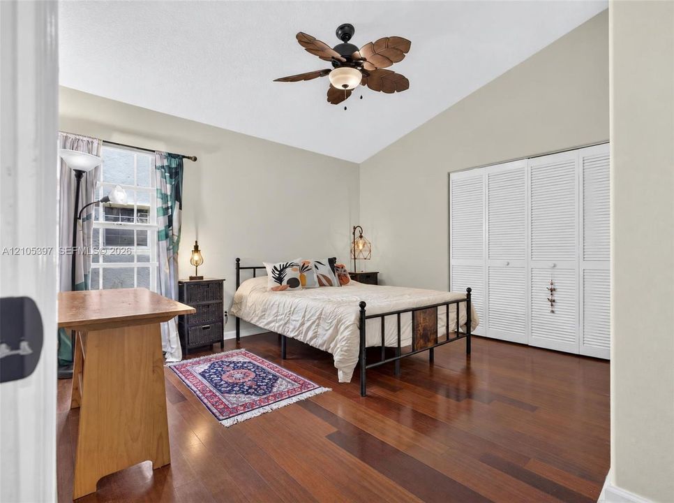 Vaulted ceiling featuring a leaf-style ceiling fan, wood-finish flooring, and white louvered bifold closet doors