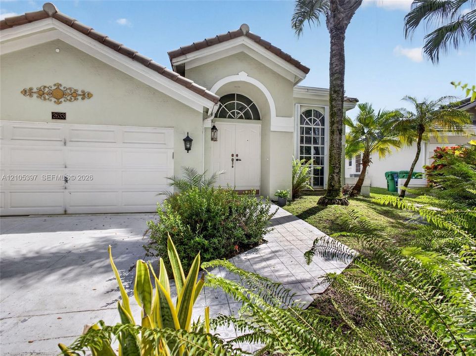 Stucco exterior featuring a 2022 tiled roof, double-entry front doors with an arched transom window, and a paved walkway