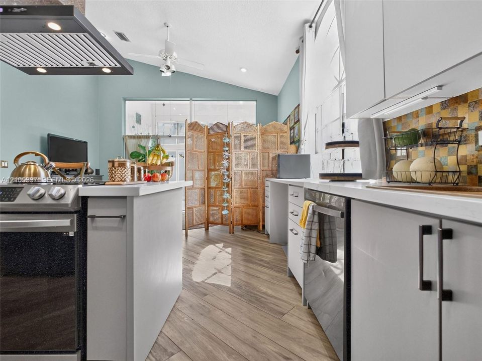 Kitchen featuring vaulted ceilings, stainless steel range with a professional-style overhead vent hood, light grey cabinetry, and mosaic tile backsplash