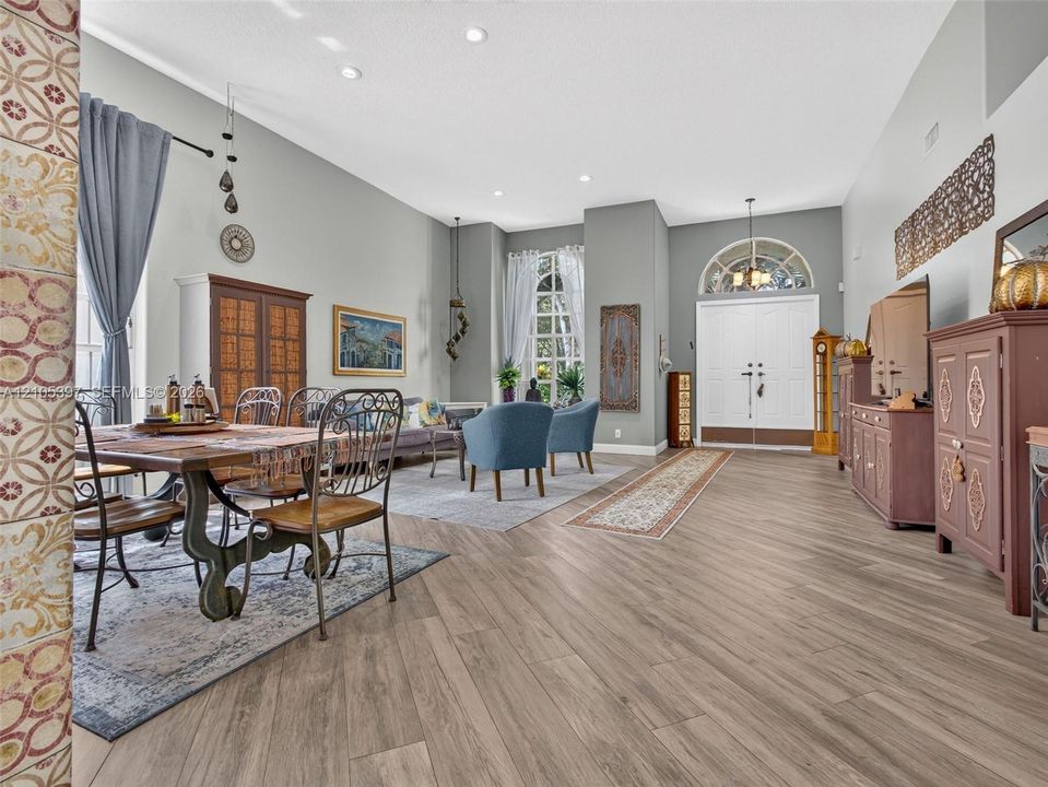 High-ceiling living and dining  area featuring wood-finish flooring, recessed lighting, double-entry doors, and expansive windows