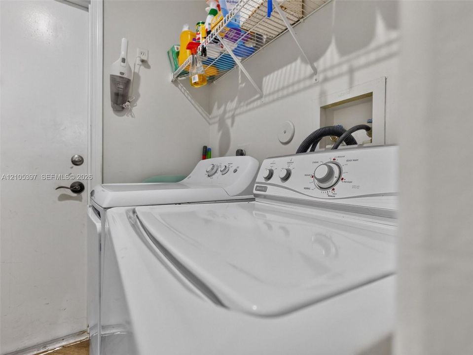 Dedicated laundry area featuring a white top-loading washer and dryer, integrated plumbing connections, and an overhead wire shelving unit