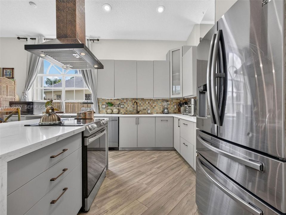 Kitchen featuring flat-panel cabinetry, quartz countertops, a copper-finish range hood, stainless steel appliances, and porcelain wood-finish flooring