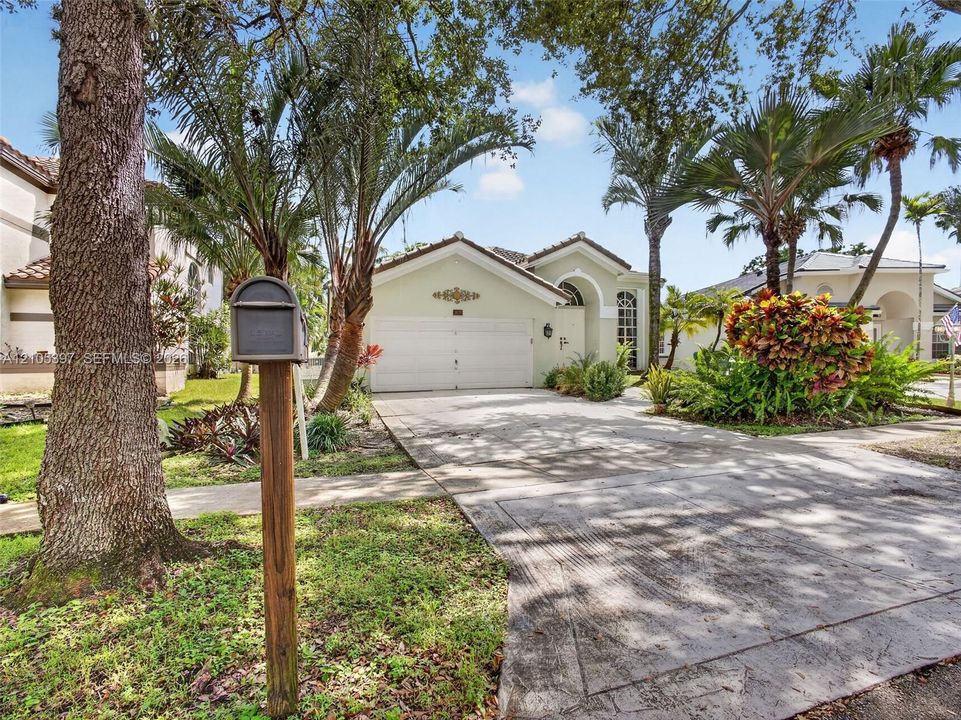 Exterior facade featuring a stucco finish, arched entryway, two-car garage, and mature landscaping