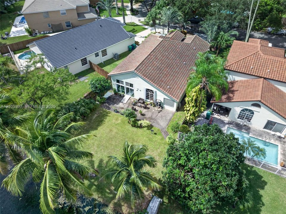 Aerial perspective of a property featuring a tiled roof, concrete patio, grass lawn, mature palm trees, and rear water frontage