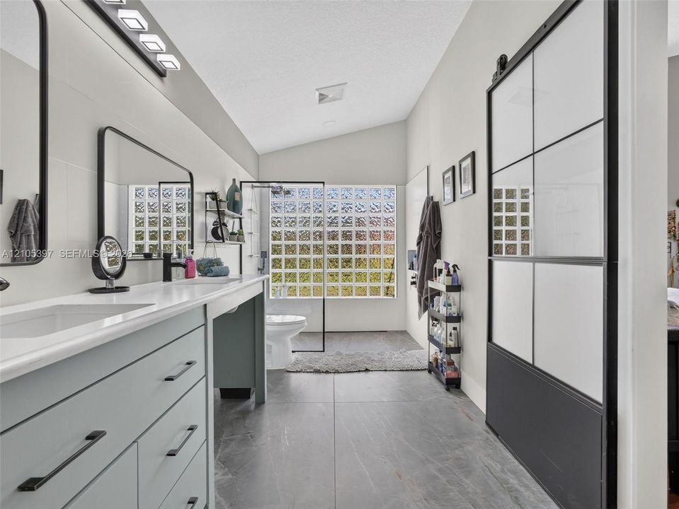 Bathroom featuring a dual-sink vanity with matte black hardware, large-format tile flooring,  and a sliding door with a black grid frame