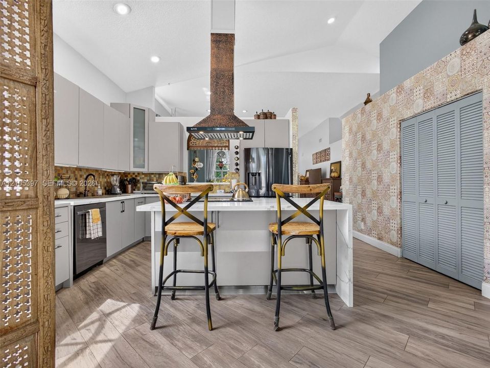Kitchen featuring flat-panel cabinetry, a waterfall-edge center island, a hammered copper range hood, and porcelain wood-finish flooring