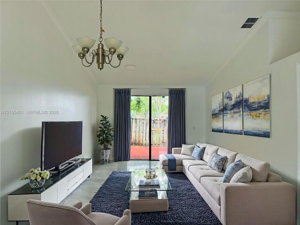Vaulted ceilings, large-format tile flooring, a multi-arm chandelier, and a sliding glass door providing access to a patio area
