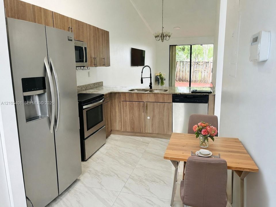 Modern kitchen featuring stainless steel appliances, wood-finish cabinetry with soft-close drawers, quartz countertops, and a matte black pull-down faucet