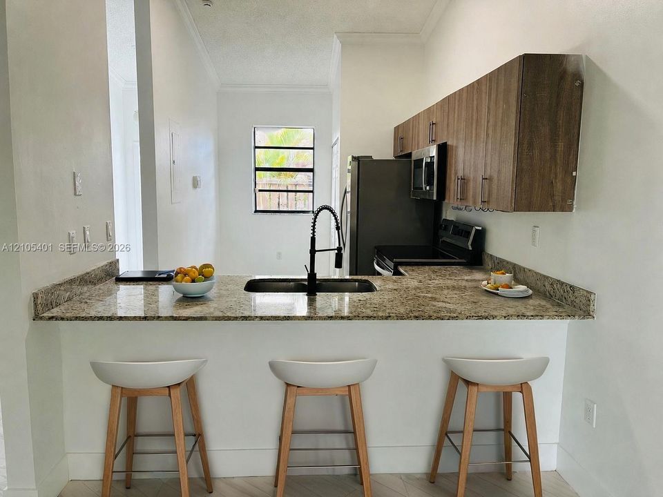 Kitchen featuring stone countertops, wood-finish cabinetry, a single-basin undermount sink with a matte black pull-down faucet, and a suite of stainless steel appliances