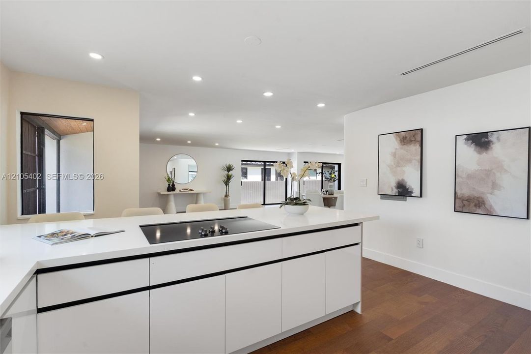Kitchen island featuring white flat-panel cabinetry, a solid surface countertop, and an integrated cooktop, complemented by recessed lighting and wood-finish flooring