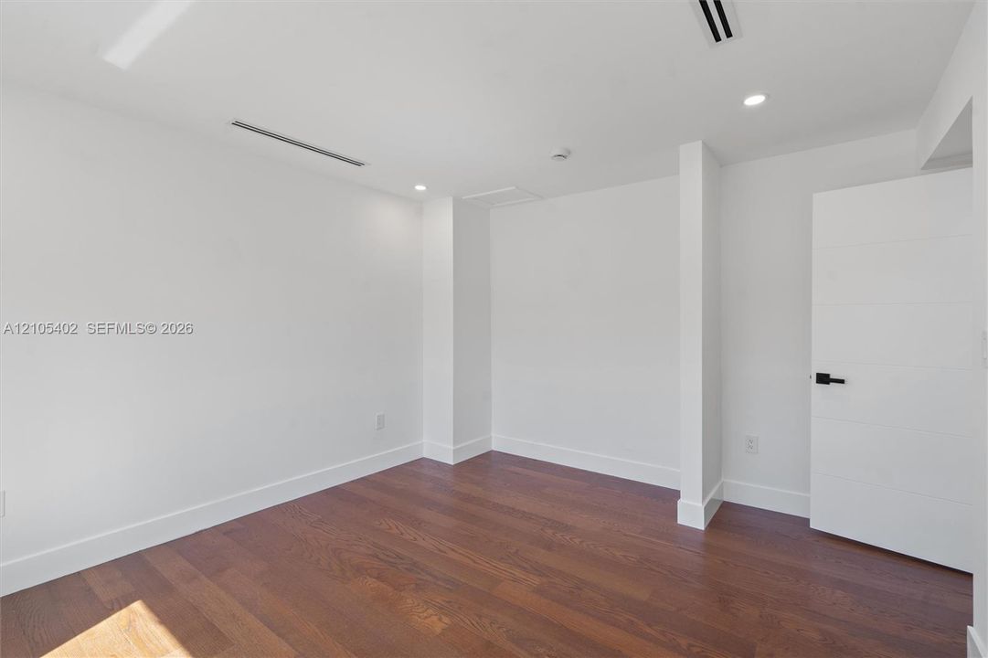 Neutral interior featuring wood-finish flooring, recessed lighting, and a multi-panel door with matte black hardware
