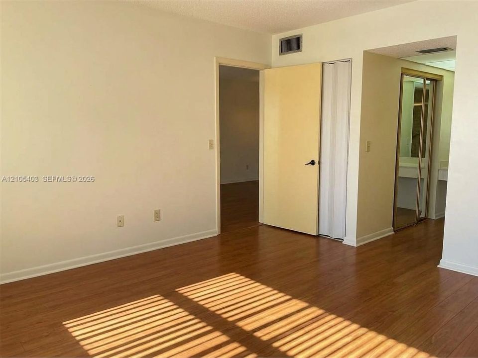 Wood-finish flooring, white painted walls, and a built-in closet with mirrored sliding doors