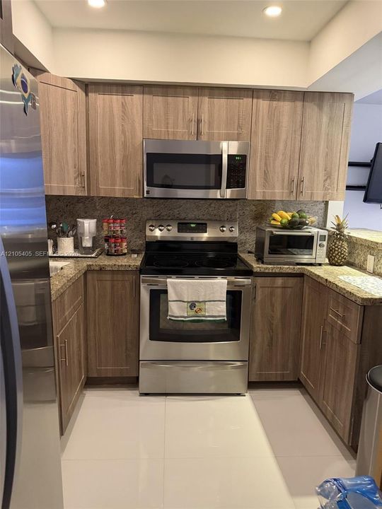 Stainless steel appliances, wood-finish cabinetry, recessed lighting, stone countertops, and a full-height stone-finish backsplash
