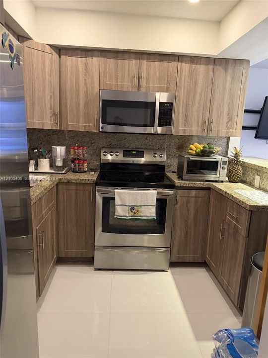 U-shaped kitchen featuring wood-finish cabinetry, stainless steel appliances, speckled countertops, and a full-height backsplash