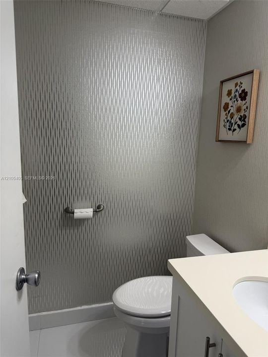 Powder room with patterned wall covering, white toilet, vanity with light-toned countertop, and integrated sink