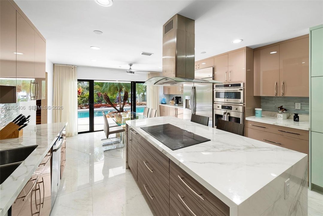 Gourmet kitchen featuring a large central island with integrated cooktop, stainless steel appliances, gloss-finish cabinetry, and a tile backsplash