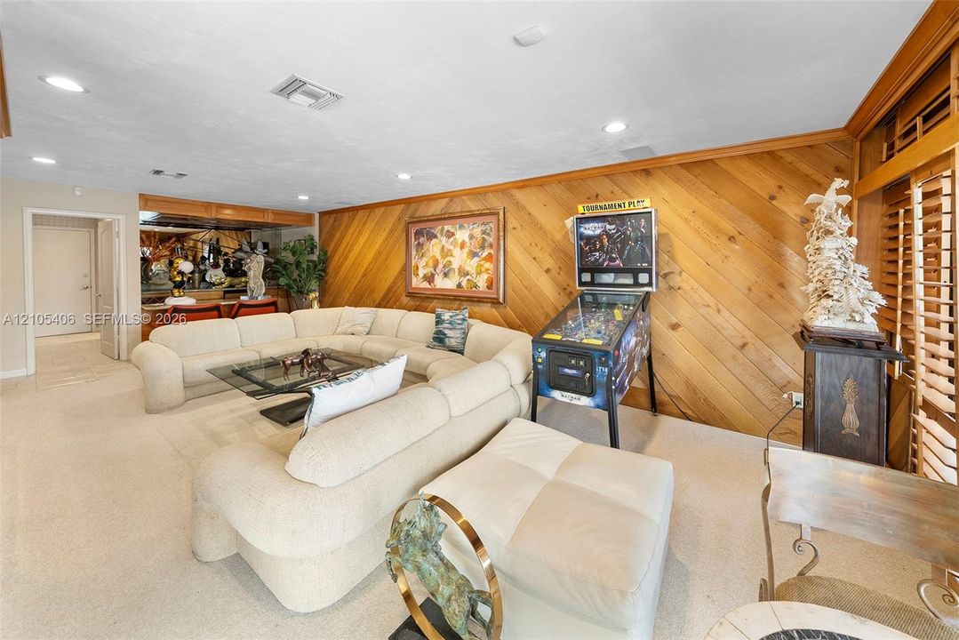 Wood-paneled wall, recessed lighting, and a built-in wet bar with mirrored backsplash