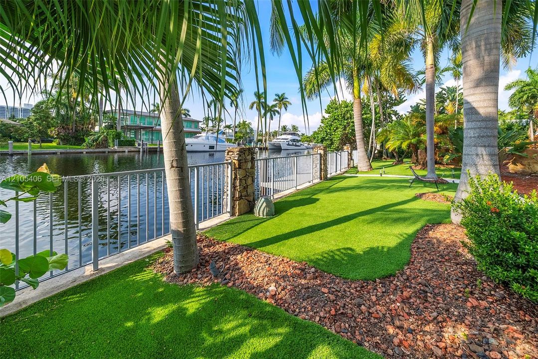 Waterfront property with a metal railing, stone column accents, and lush artificial turf