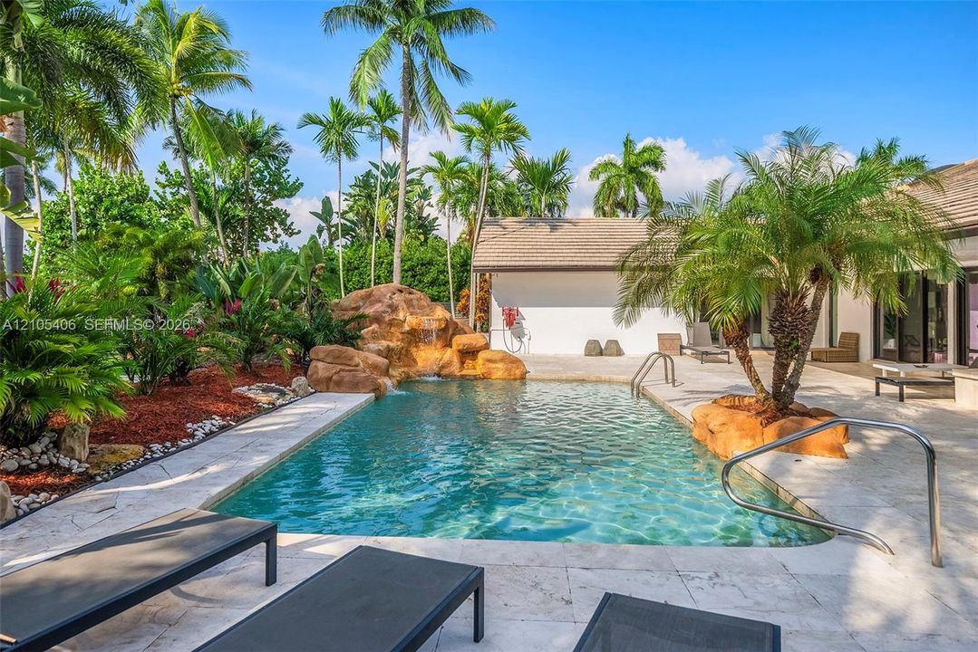 Swimming pool with rock waterfall feature, integrated palm trees, and surrounding hardscaping
