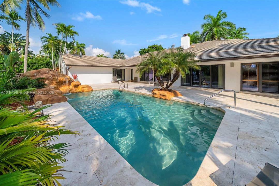 Rectangular swimming pool with rock waterfall feature, integrated steps, and surrounding patio