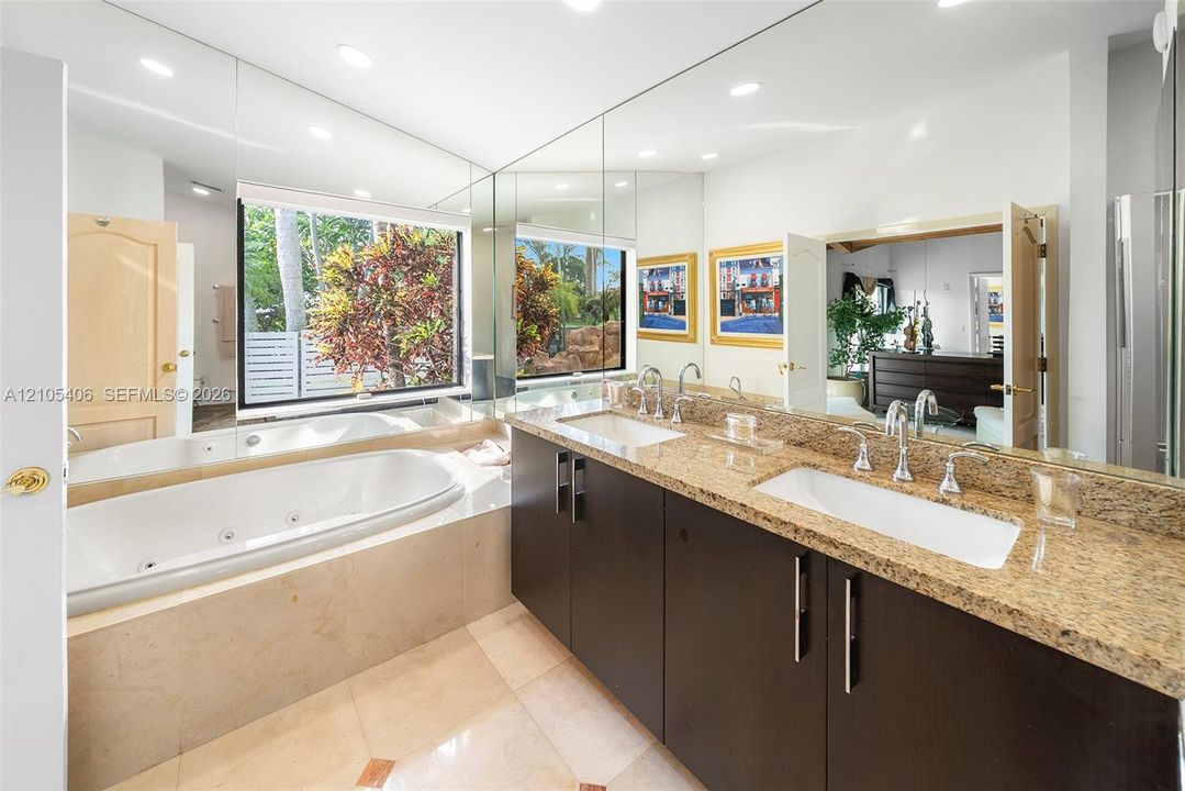 Dual vanity with stone countertops and undermount sinks, full-height wall mirrors, built-in soaking tub, and large window
