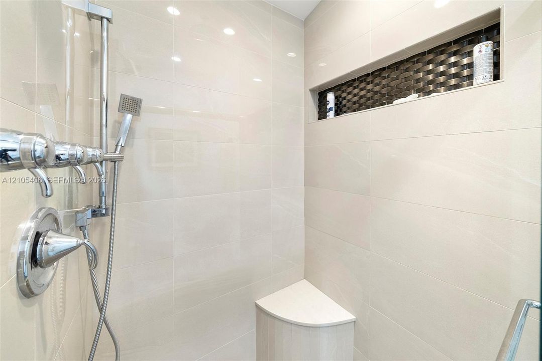 Shower with polished chrome fixtures, integrated niche with mosaic tile accent, a built-in corner bench, and large format wall tiling