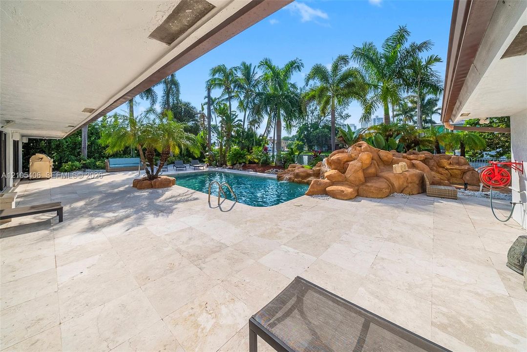 Expansive outdoor living area featuring a large swimming pool, rock water feature, and extensive patio paving