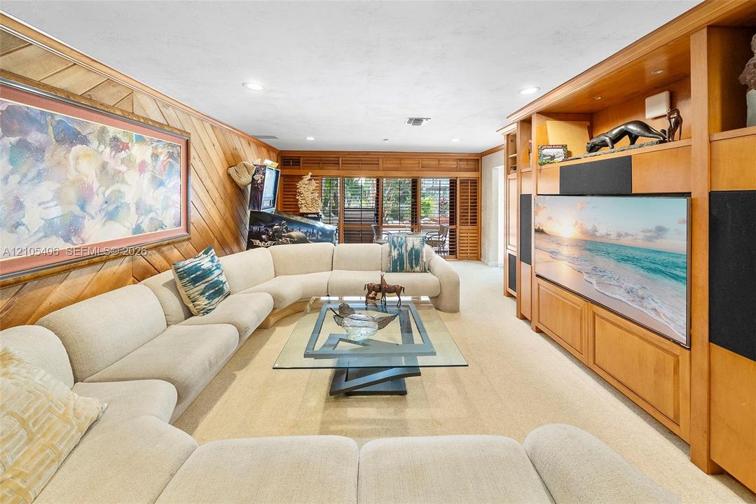 Wood-paneled wall, recessed lighting, built-in media center, plantation shutters, and light-toned carpet