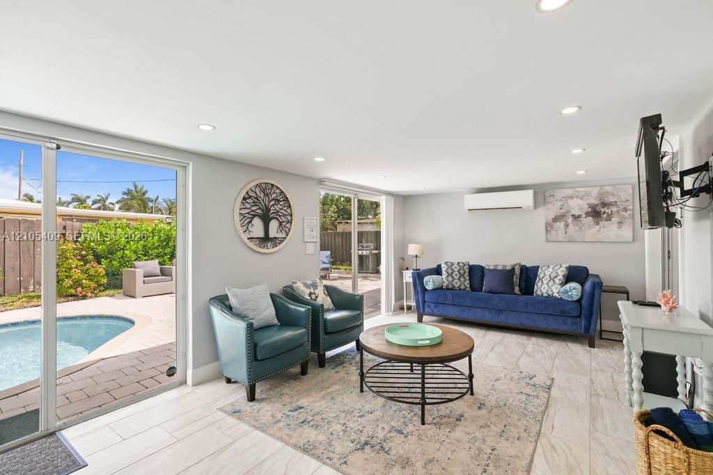 Recessed ceiling lighting, mini-split air conditioning unit, light-toned tile flooring, and sliding glass doors opening to a paved patio and in-ground swimming pool