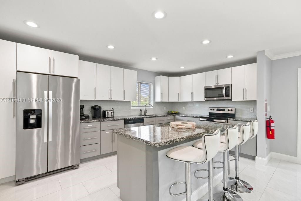 Kitchen featuring stainless steel appliances, granite countertops, white upper cabinetry, grey base cabinetry, and recessed lighting
