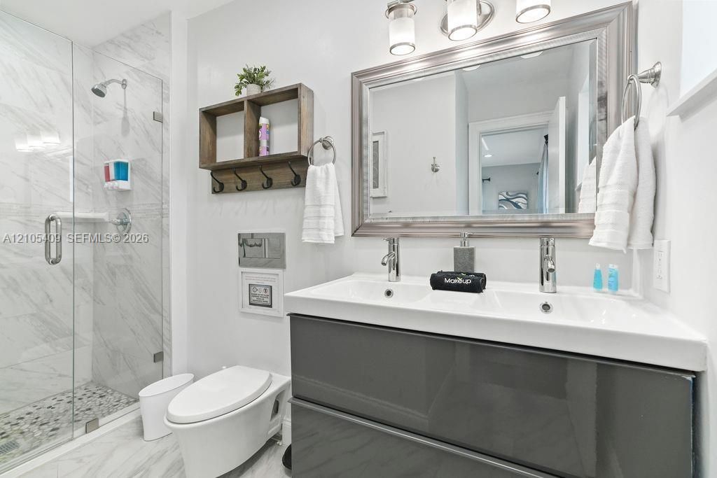 Glass-enclosed shower with white marble-look tile and pebble-style floor