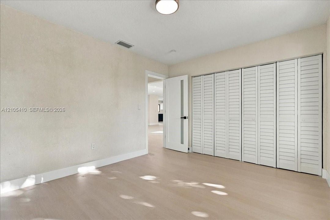 Room featuring light-toned wood-finish flooring, white louvered-panel closet doors, and a single-panel door with a frosted glass insert