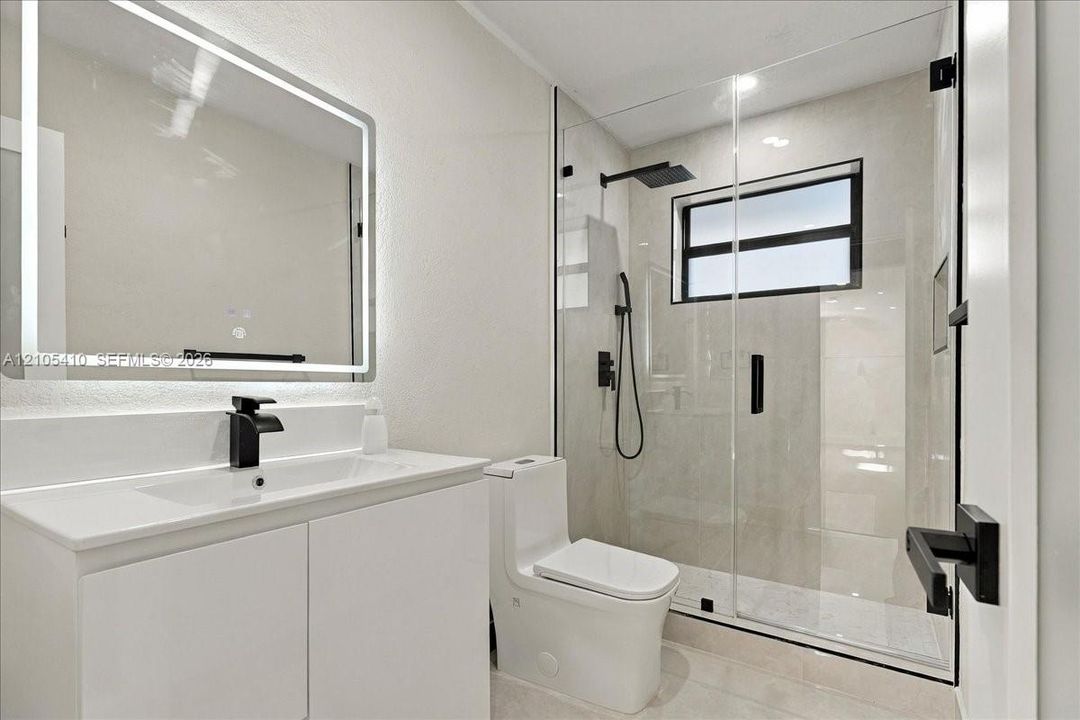 Bathroom featuring a white vanity cabinet, rectangular under-mount sink, integrated LED mirror, walk-in shower with glass enclosure, and matte black hardware