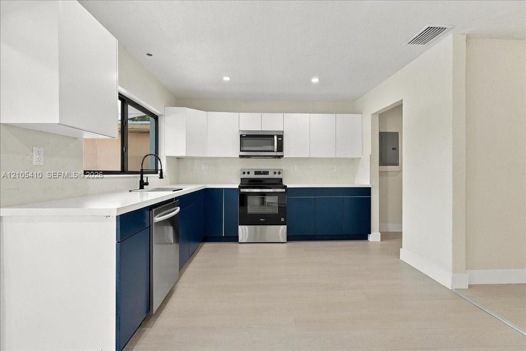 Kitchen featuring two-tone cabinetry, solid surface countertops, stainless steel appliances, and wood-finish flooring