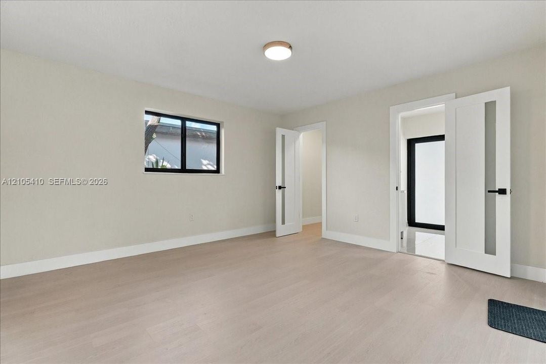 Interior space featuring light wood-finish flooring, neutral wall paint, modern doors with frosted glass panels and matte black hardware, and a flush-mount light fixture