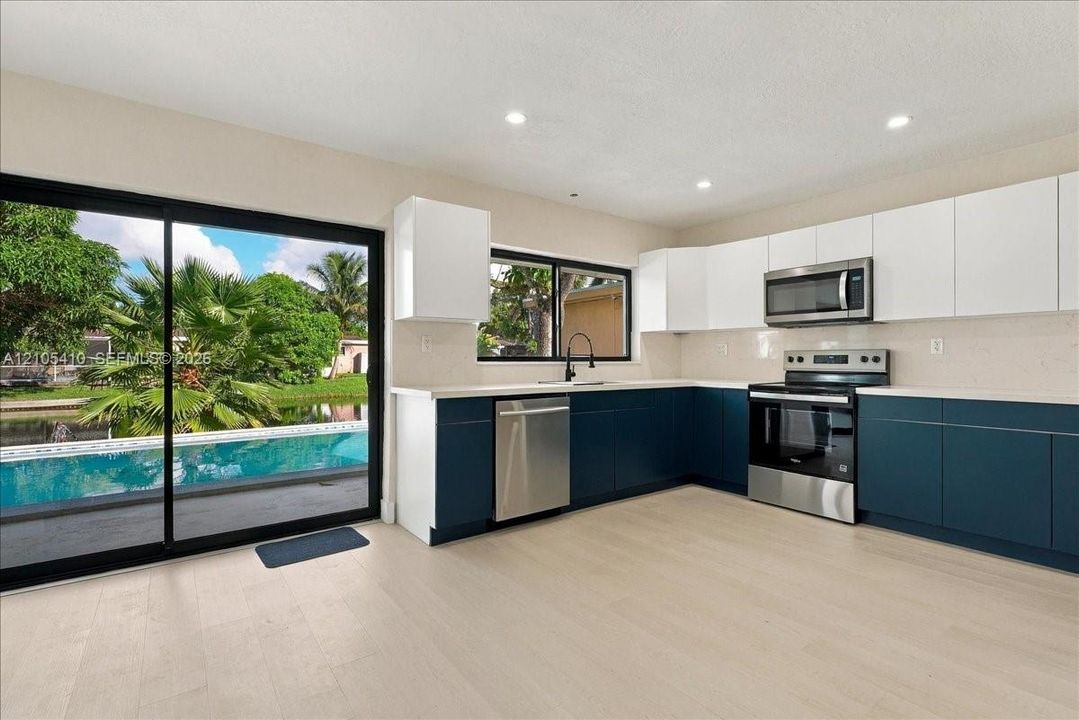 Kitchen featuring two-tone cabinetry, stainless steel appliances, light-toned wood-finish flooring, quartz countertops, and floor-to-ceiling sliding glass doors