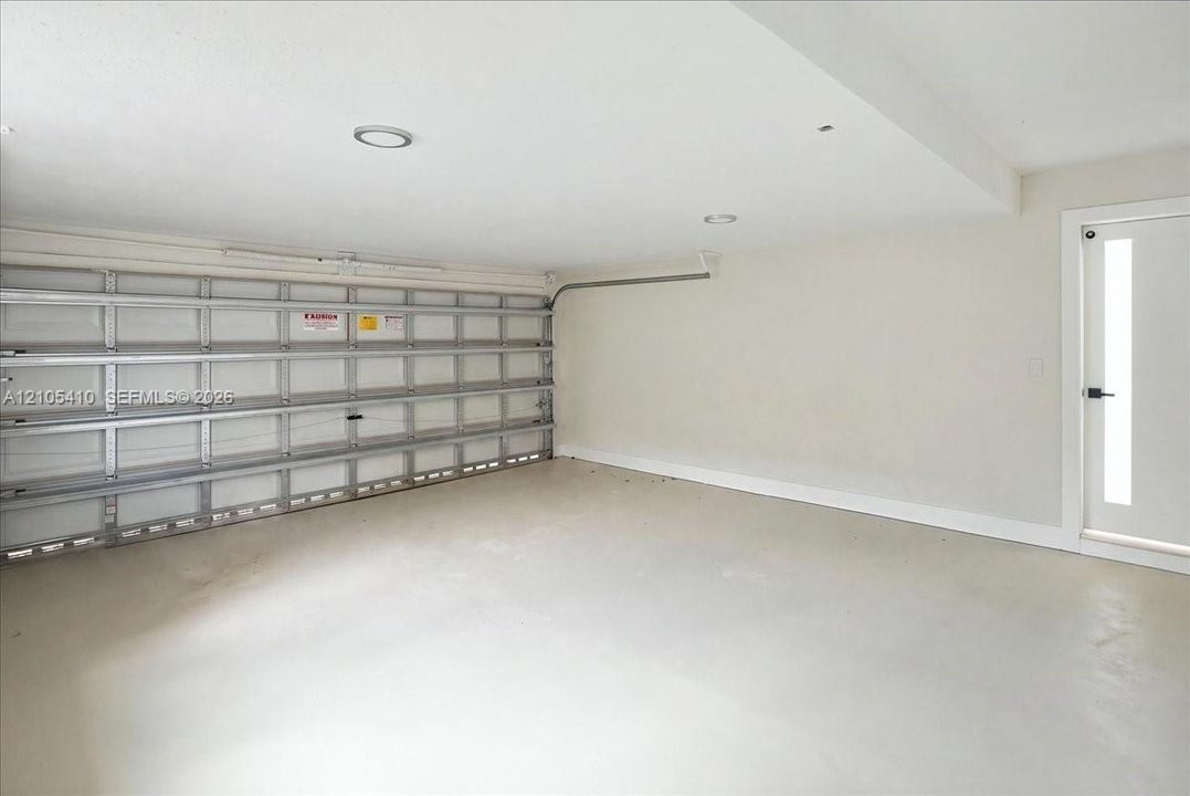 Enclosed garage space featuring a metal sectional door, recessed lighting, smooth concrete flooring, and a glass-paneled entry door with matte black hardware