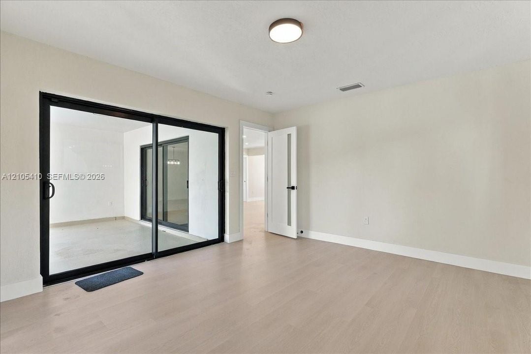 Neutral-toned interior featuring wood-finish flooring, sliding glass doors with black frames, and a modern interior door with glass inlay