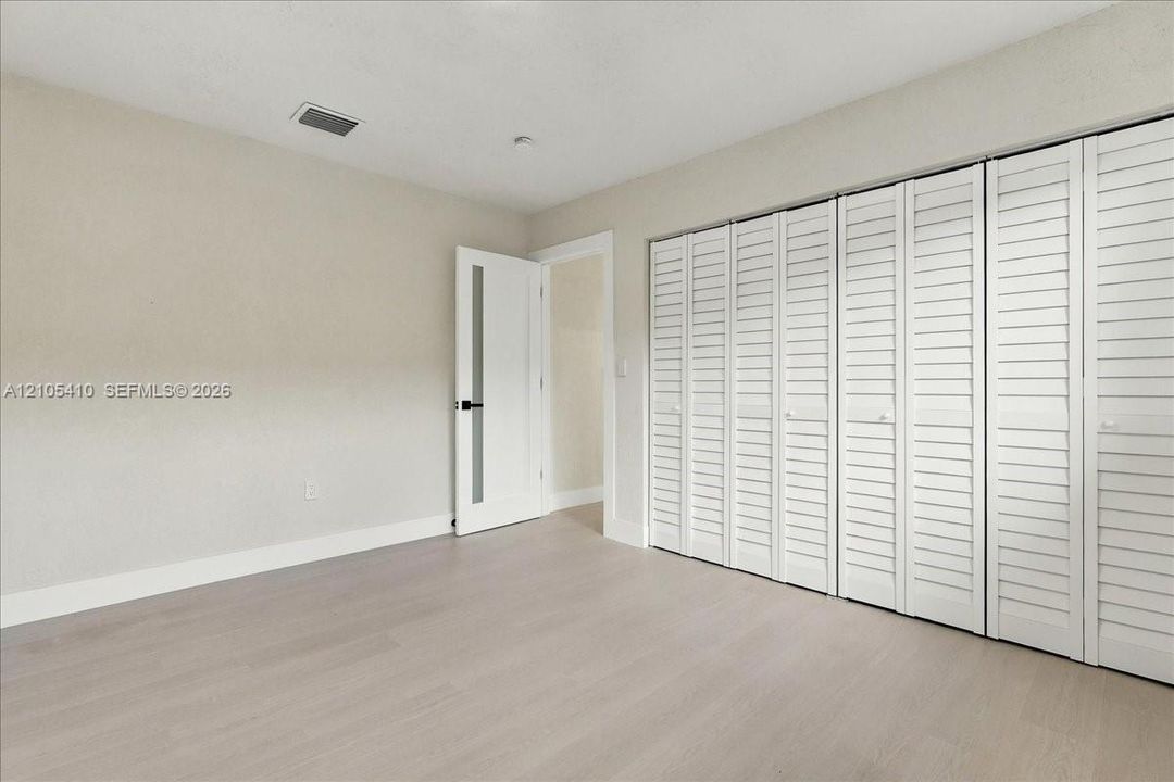 Light-toned wood-finish flooring, white louvered bifold closet doors, and a single-panel interior door featuring a vertical frosted glass insert with matte black hardware