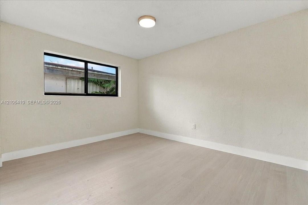 Neutral-toned room featuring wood-finish flooring, a single-pane horizontal window with a dark frame, and a circular flush-mount ceiling light