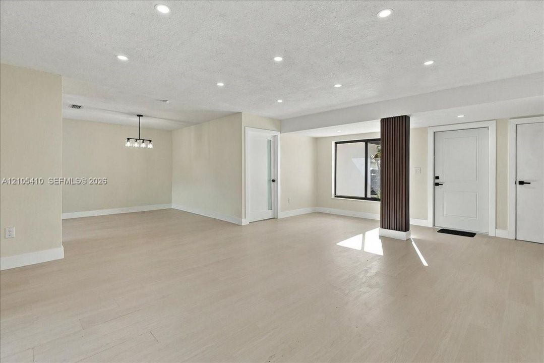 Open-concept interior featuring light wood-finish flooring, recessed lighting, a decorative vertical slat support column, and a modern multi-light chandelier