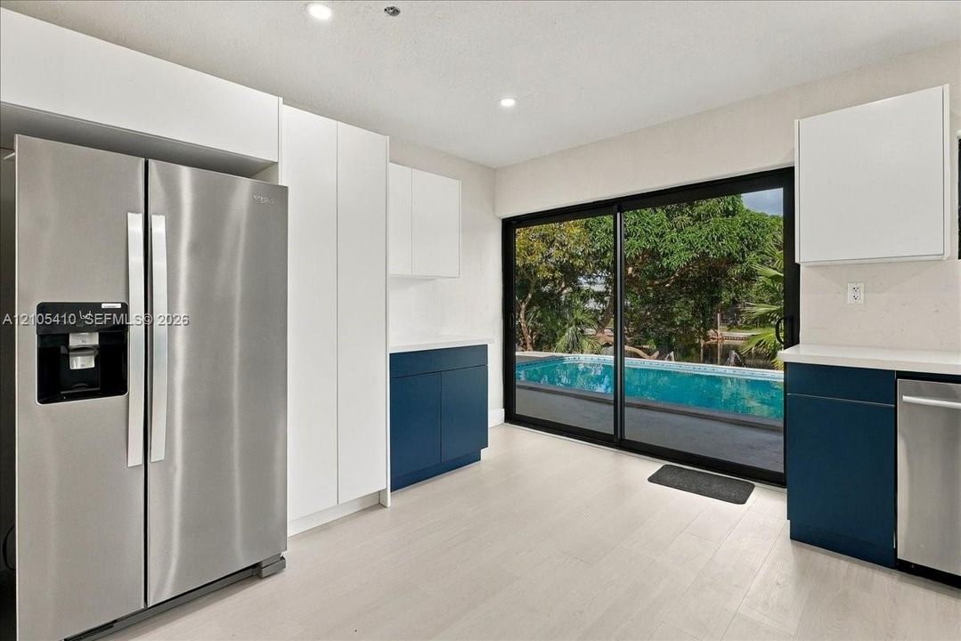 Kitchen featuring white and navy cabinetry, stainless steel appliances, light wood-finish flooring, and sliding glass doors with a perspective of an outdoor pool