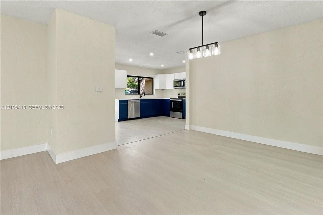 Open interior featuring light-tone wood-finish flooring, a contemporary five-light linear pendant fixture, and a kitchen equipped with dual-tone cabinetry, stainless steel appliances, and tile flooring